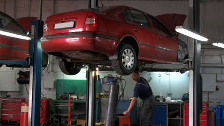 Car is being lifted down by hydraulic machine for technician. Close-up red car with opened hood.の写真素材