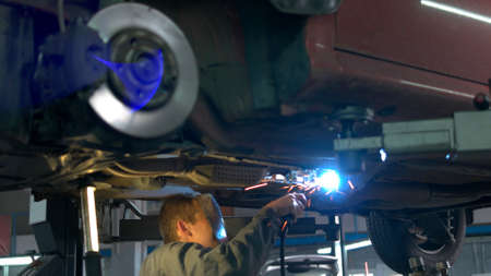 Close-up welding work on a lifted car. View from the back. Mechanic welds the bottom of the car.