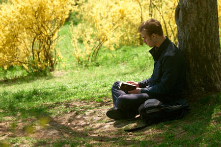 26.04.2019 - Kyiv, Ukraine. Young man reading the Bible in the park. Beautiful spring nature in the...