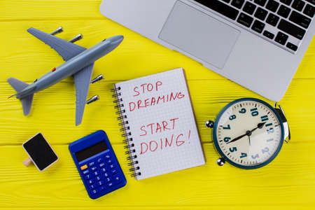 Flat lay travel and finance concept. Stop dreaming start doing. Airplane, calculator, alarm clock and laptop.の写真素材