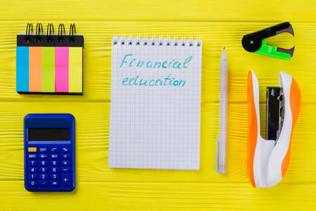 Financial education concept flat lay. Notepad with pen and other stationery items on yellow wooden...