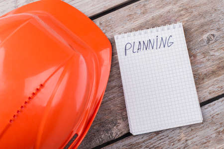 Planning counstructor building concept. Worker's helmet and notepad on aged wooden table.の写真素材