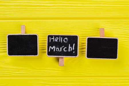 Three small nameplates on a yellow wooden table. Hello march concept.の写真素材