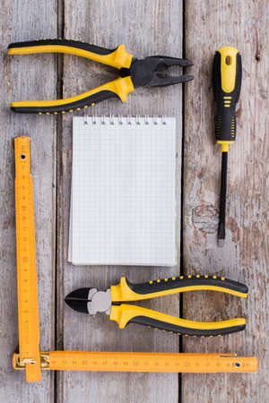 Constructor or repairman accessories and blank notepad. Top view flat lay. Old wooden table surface.