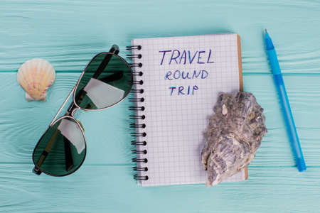 Planning a trip around the world. Notebook,seashells, aviator glasses on a blue wooden background.