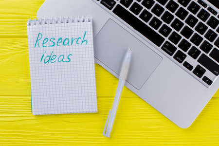 Notepad with research ideas and pen. Laptop keyboard on yellow wood.の写真素材