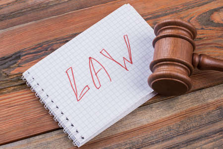 Close-up laws words written on spiral notepad and gavel. Brown textured table.