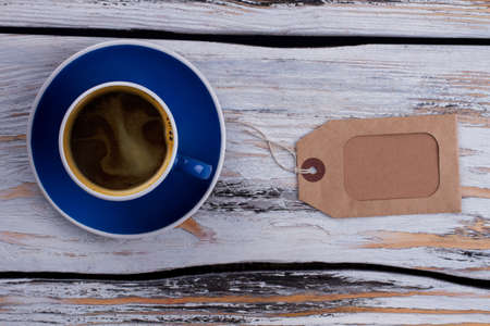 Cup of coffee on blue plate and morning beige tag. Old white vintage wood on background.の写真素材