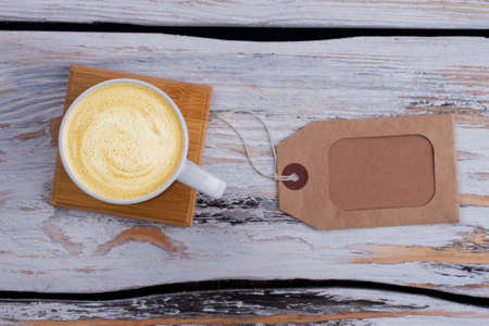 White mug of coffee with foam and morning tag. Topview from above. White wooden background.の写真素材