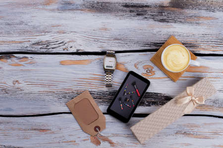 Flat lay adult man accessories. Coffee, gift box, luxury clock and paper tag. White wooden...