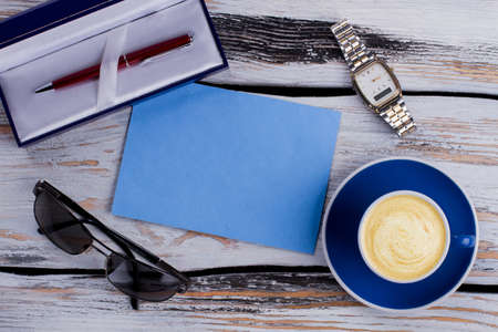 Flat lay morning blue paper with cup of coffee and sunglasses. Writer's accessories top view. White woo on background.の写真素材
