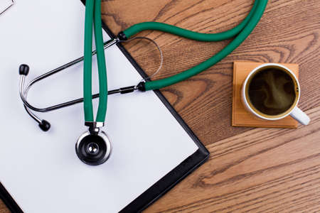 Topview cup of coffee with clipboard and stethoscope. Brown wooden background.の写真素材
