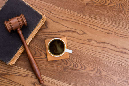 Old vintage book with judge hammer and cup of coffee. Brown wooden background.の写真素材
