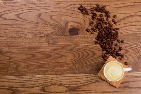 Cup of cappuccino or latte and spilled coffee beans. Brown rustic wooden background. Topview flat lay copy space.の写真素材