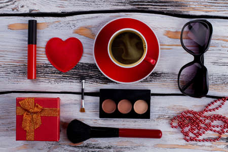 Flat lay red female accessories on white vintage table. Topview cup of coffee, bead necklace, sunglasses, gift box and brush with powder.の写真素材