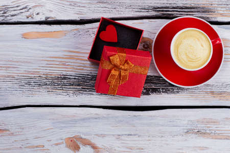 Opened gift box and cup of coffee with foam. Topview flat lay. White wood on background.の写真素材