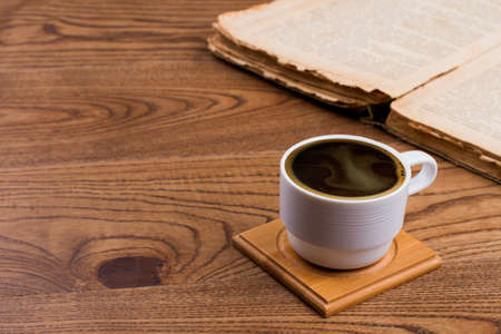 White cup of coffee and opened book. Brown wooden table.の写真素材