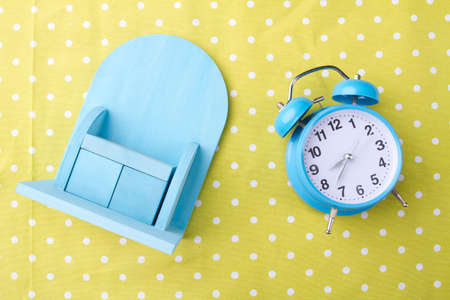 Miniature cupboard and alarm clock on yellow background. Morning time concept. Flat lay photo.