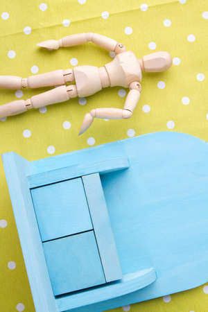 Small toy furniture and doll. Miniature human mannequin figure and miniature blue cupboard on yellow background.の写真素材
