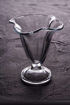 Empty glass ice cream dish. Dessert glassware on a raised grunge dark surface.