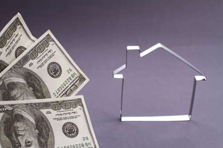 Concept investment in property. Metallic house outline frame and fan of dollars on grey background.