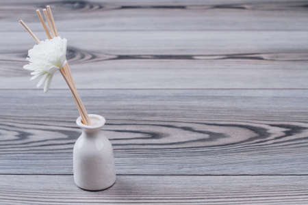 The white vase with artificial flowers and wooden sticks. Grey wooden background.