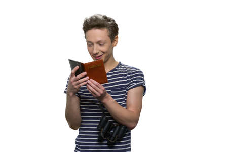 Male caucasian teenage traveler is looking at opened passport. Isolated on white background.