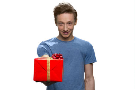 American teenage boy is giving red gift box. Isolated on white background.