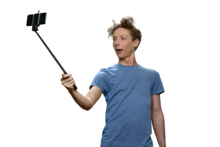 Portrait of teenage boy is taking selfie on his smartphone. Isolated on white background.の写真素材