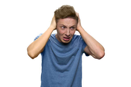 Teen boy is suffering from terrible headache. Pourtrait of young guy touching his head with both hands because of a pain. Isolated on white background.の写真素材