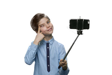 Boy with grimace making a selfie on white background. Holding stick for making photo with smartphone.の写真素材