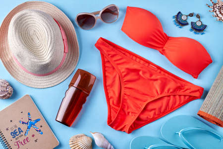 Female beach resort accessories. Bathing suit with straw hat, sunglasses and sun cream on blue background.の写真素材