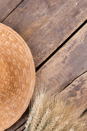 Vintage table with wheat spikelets and straw hat. Straw hat and wheat ears on cracked wooden background, top view. Space for text.の写真素材