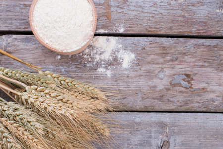 Bowl with flour and ears of wheat. Ears of wheat and bowl of flour on rustic wooden boards. Space...