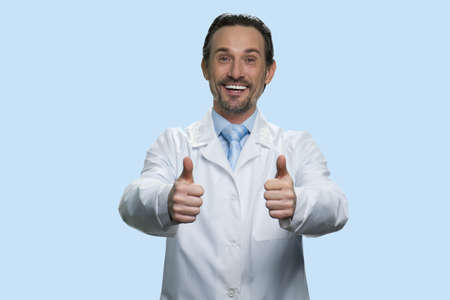 Cheerful scientist doctor giving two thumbs up. Happy smiling pharmacist in white coat against light blue background. Great success concept.の写真素材