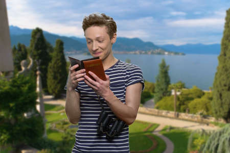Happy teen boy looking at his passport. Sea and beautiful nature in the background. Travel concept.