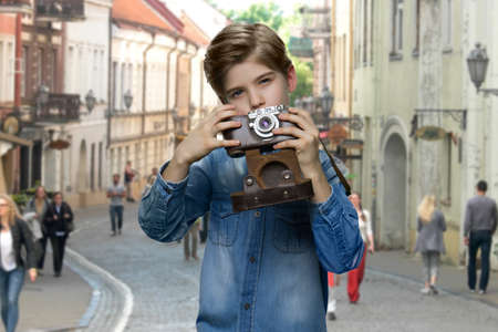 Little boy using vintage camera outdoor. Boy traveler in denim jacket taking picture with old retro camera. Tourism concept.の写真素材