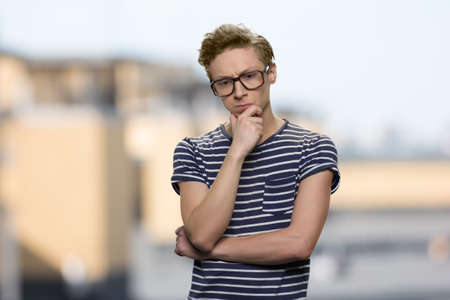 Pensive guy wearing eyeglasses touching chin.Thoughtful nerd boy on abstract blurred background. Serious face expression.の写真素材