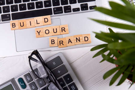 Flat lay build your brand slogan on a tablet pc touchpad. Calculator with glasses and plant. Isolated on white background.の写真素材