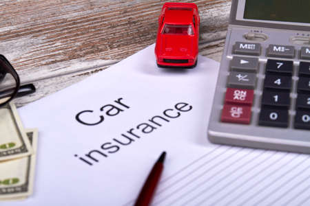 Car insurance concept. Red toy car with opened copybook, calculator and pen on wooden table.