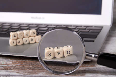 Looking through a magnifying glass on seo blocks. Wooden cubes with letters on the laptop. Link...