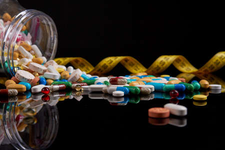 Concept of weight loss using medicine. Close up of different drugs, pills, capsules and measure tape...