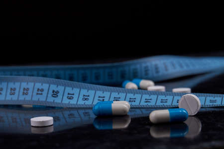 Medicine for weight loss. Blue measure tape and capsule pills close-up.の写真素材