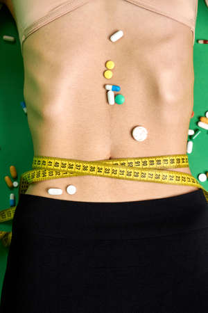 Slim womans waist wrapped with measure tape. Pills on a female stomach. Concept of weight loss using madicine.の写真素材