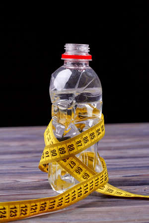 Bootle of water with measure tape. Weight loss and diet concept. Sporty bootle is tied with yellow measure tape on wooden background.の写真素材