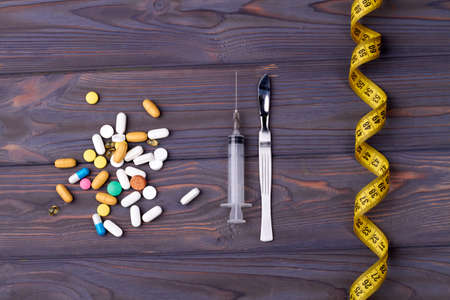Concept of weight loss using medicine. Pile of drugs, pills, capsules with syringes and measure tape on the wooden table.の写真素材