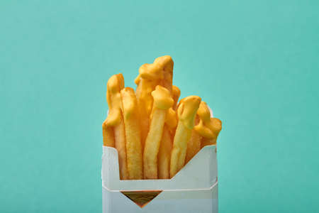 Close up fries with yellow sauce in a pack of cigarettes. Concept on unhealthy harmful food. Isolated on turqouise background.の写真素材