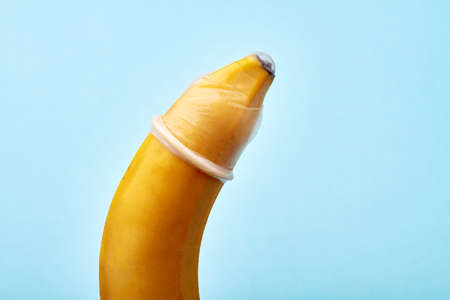 Sexual education concept. Close up big ripe banana with condom isolated on blue background.