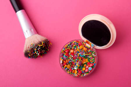 Cosmetic powder case with sweet sprinkles. Make-up brush with case with sweet candies isolated on pink background.の写真素材