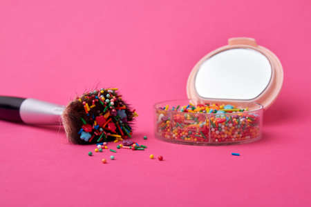 Make-up accessories with sweet sprinkles. Cosmetic powder case with brush covered with candies. Isolated on pink background.の写真素材